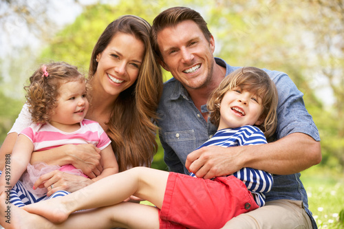 Parents Sitting With Children In Field Of Summer Flowers