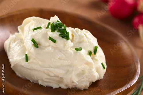 Fresh cream cheese spread on wooden plate with chives