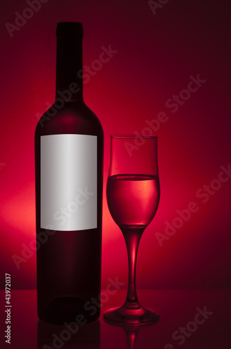 bottle and glass with white wine on red background
