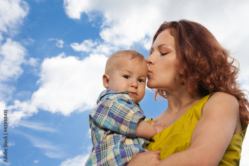 mother kissing her baby on cloudy background mother kissing her baby on cloudy background