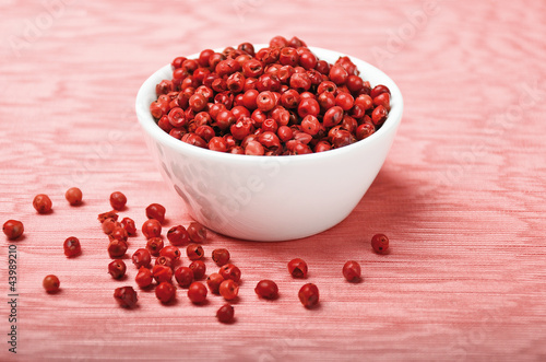 Pink pepper. Dried pink peppercorns in a white porcelain bowl on pink textile made of linen. Schinus berries. Macro photo.