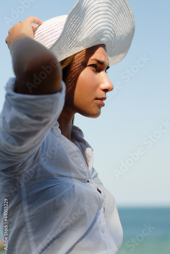 Young woman resting by the sea and wearing white hat photo