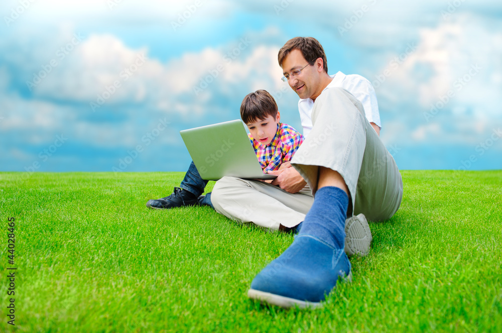 Father and son at park smiling and having fun with laptop Father and son at park smiling and having fun with laptop