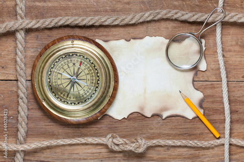 Compass, burnt paper, pencil, magnifying glass and rope on wood photo