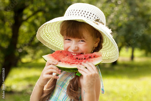 Girl in the hat and dress eating a watermelon