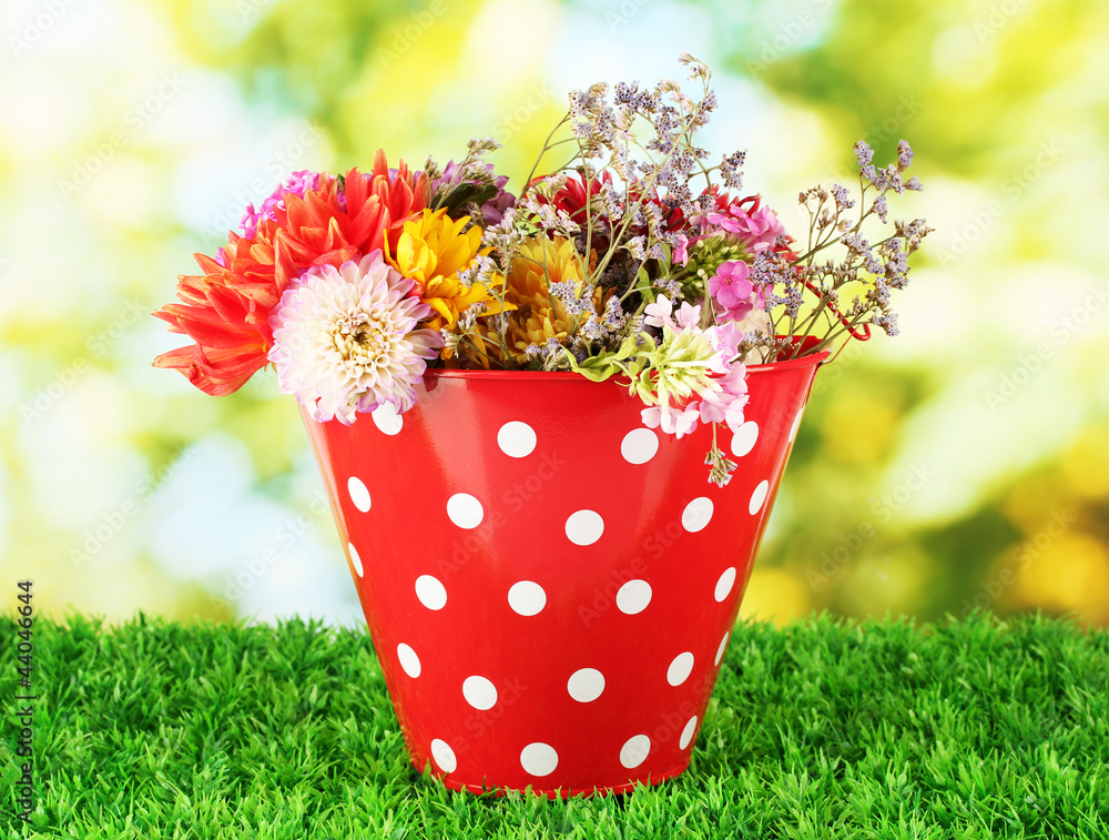 Red bucket with white polka-dot with flowers on green