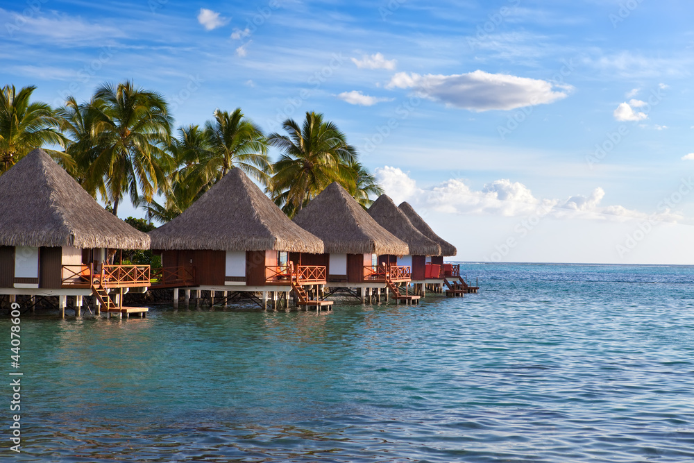 Seacoast with palm trees and small houses on water on a sunset Seacoast with palm trees and small houses on water on a sunset