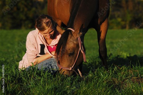 a girl sitting in the pasture beside her grazing horse