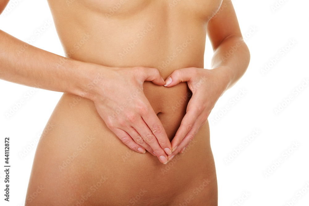 Naked belly of young woman with hands showing shape of heart.