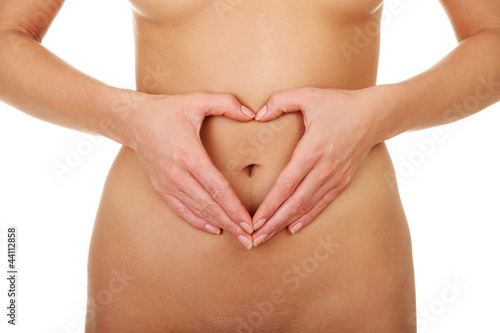 Naked belly of woman with hands showing shape of heart.