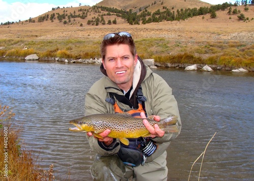 Man holding a brown trout caught fly fishing on a stream
