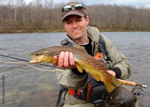 Fly fisherman with Brown Trout, fly rod and reel, in a river