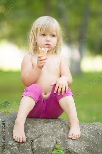 Adorable girl eat ice cream sitting on stone in park