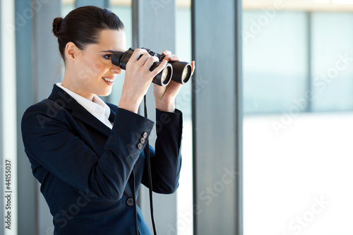 businesswoman looking outside office window with binoculars