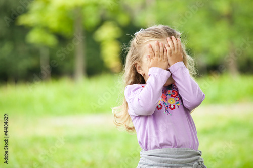 little girl is playing hide-and-seek hiding face