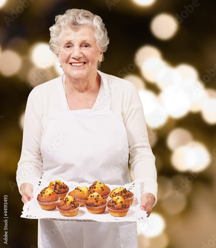 portrait of cook senior woman holding a chocolate muffins tray a