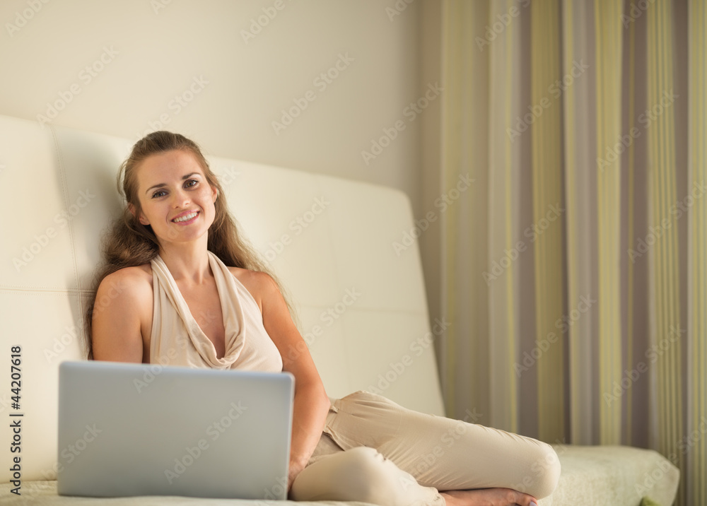 Portrait of happy young woman sitting on couch with laptop Portrait of happy young woman sitting on couch with laptop