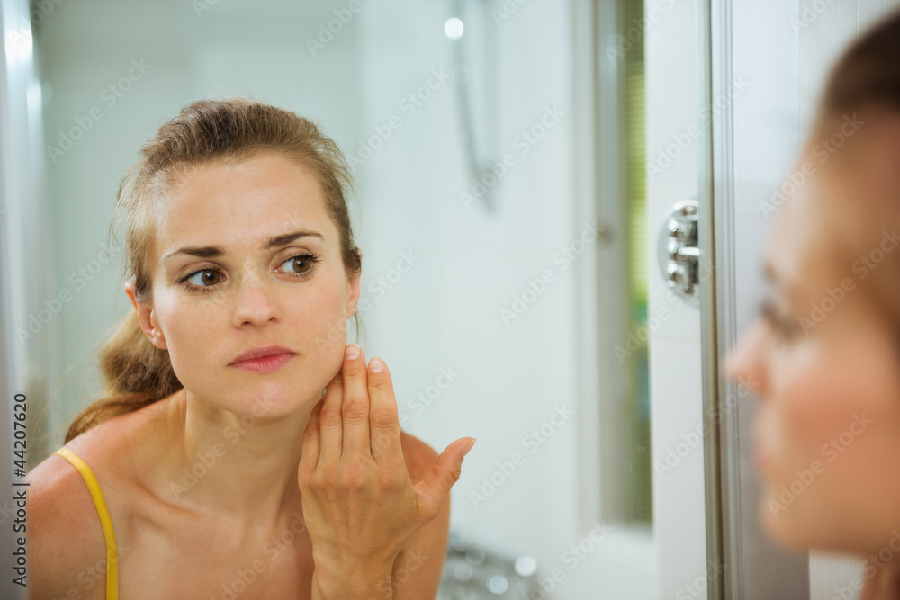 Young woman checking her face in mirror in bathroom Young woman checking her face in mirror in bathroom