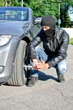 Man in mask punctures a car tyre. Revenge concept