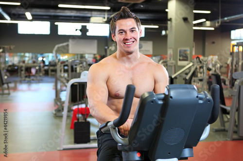 Cheerful young fitness guy working out on exercise bicycle