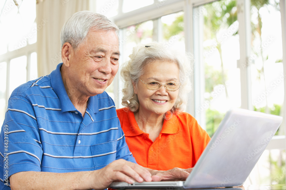 Senior Chinese Couple Sitting At Desk Using Laptop At Home Senior Chinese Couple Sitting At Desk Using Laptop At Home