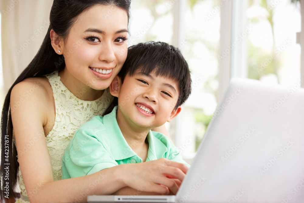 Chinese Mother And Son Sitting At Desk Using Laptop At Home Chinese Mother And Son Sitting At Desk Using Laptop At Home