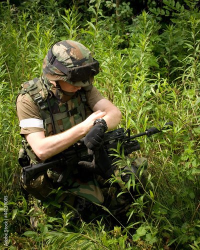 Soldier on the war in sunny day with gun in green bushes check t photo