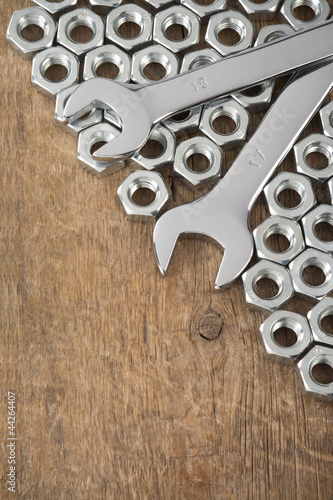 metal nuts and wrench tool on wood background