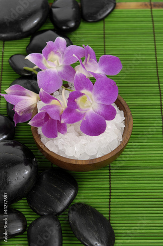 Pink orchid with herbal salt in bowl and stones on green mat