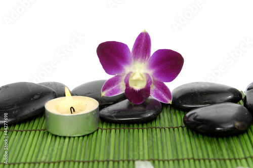 Beautiful orchid with stones and candle on green stick straw mat