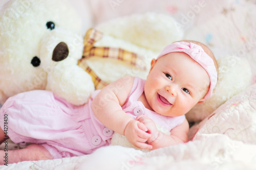 pretty smiling baby girl and teddy bear at the bed