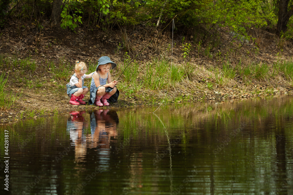 Little girls are fishing on lake in forest Little girls are fishing on lake in forest