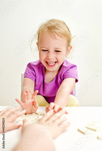 Cute little girl with mother playing domino at the table
