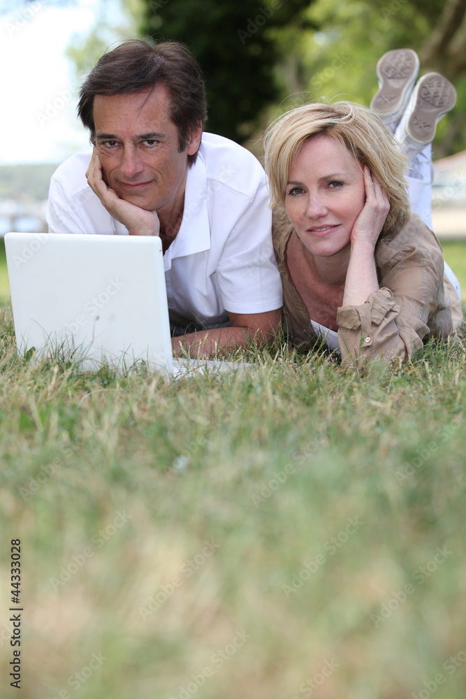 couple lying in grass using laptop couple lying in grass using laptop
