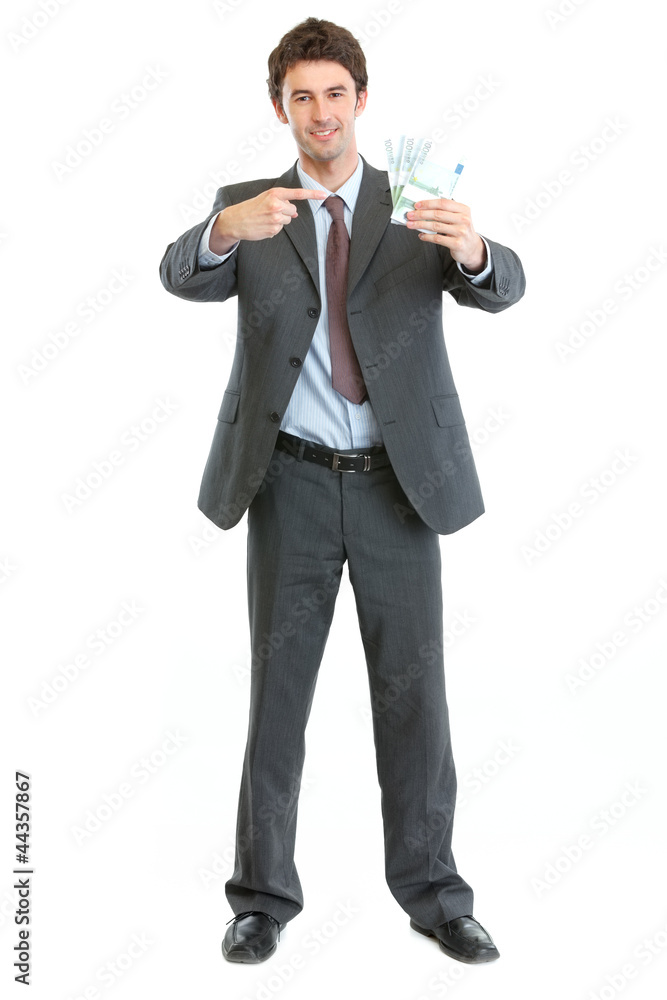Full length portrait of businessman pointing on packs of euros Full length portrait of businessman pointing on packs of euros