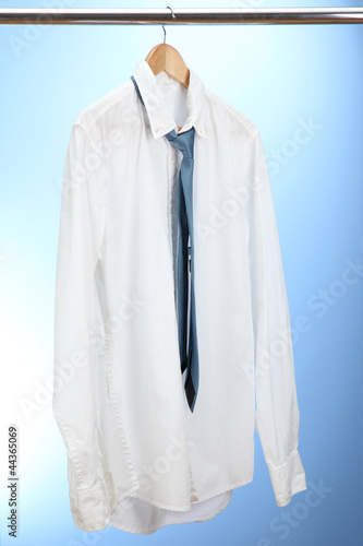 shirt with tie on wooden hanger on blue background