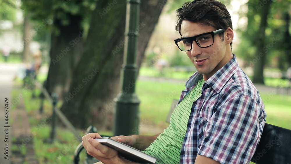 Young happy man reading book in the park, steadicam shot Young happy man reading book in the park, steadicam shot