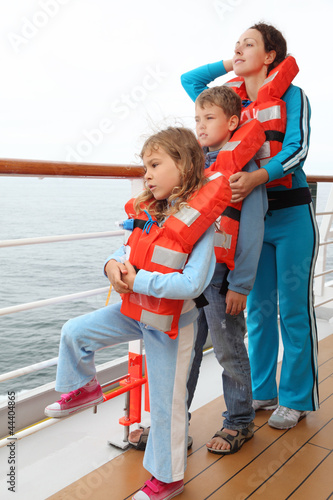 Mother, son and daughter wearing in orange life jackets stand