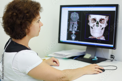 Dentist carefully looks jaw and skull X-rays at computer monitor