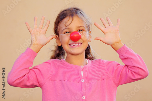 Beautiful girl wearing pink blouse with red clown nose smiles photo