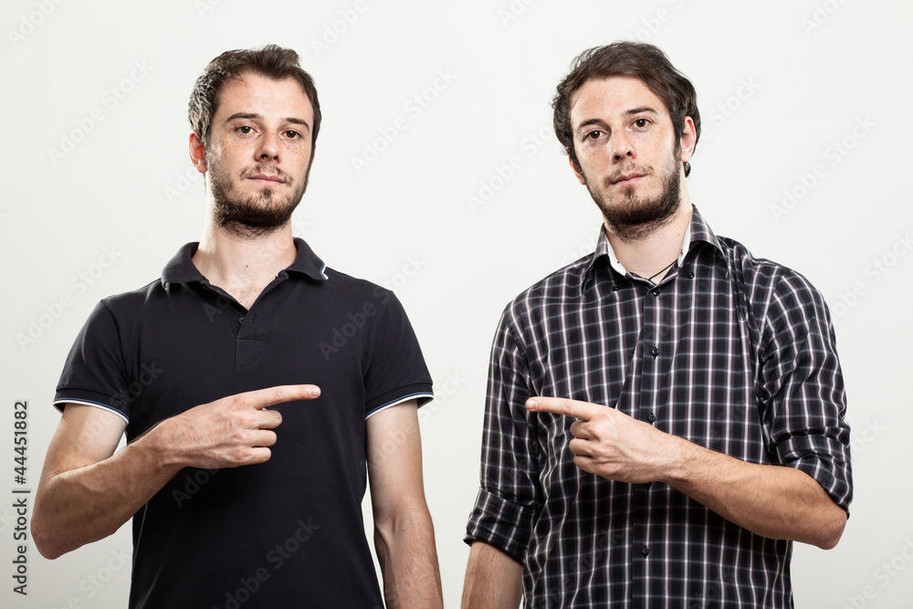 Two Serious Twins Pointing Each Other - obrazy, fototapety, plakaty 