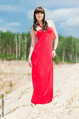 A girl in a red dress posing on a sand dune.