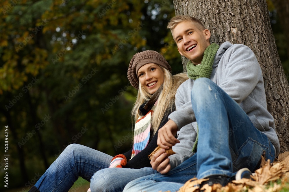 Fototapeta premium Attractive couple sitting on ground in autumn park