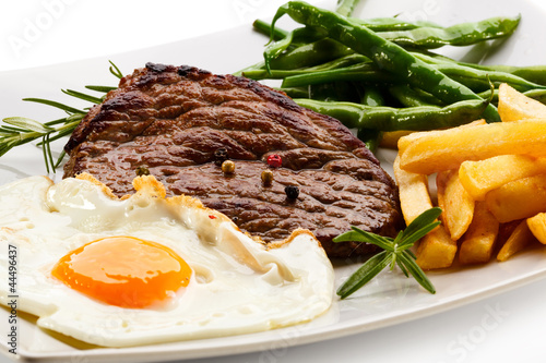 Grilled steaks, French fries, fried egg and vegetables