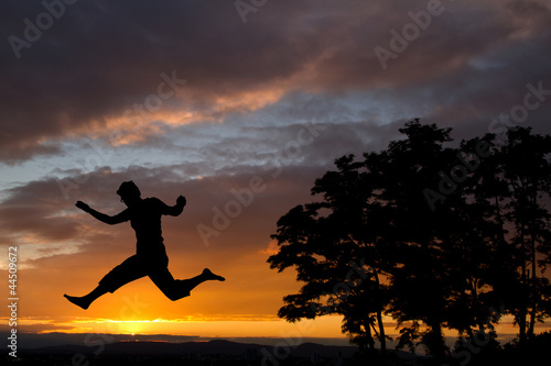 silhouette of man jumping in front of trees in sunset
