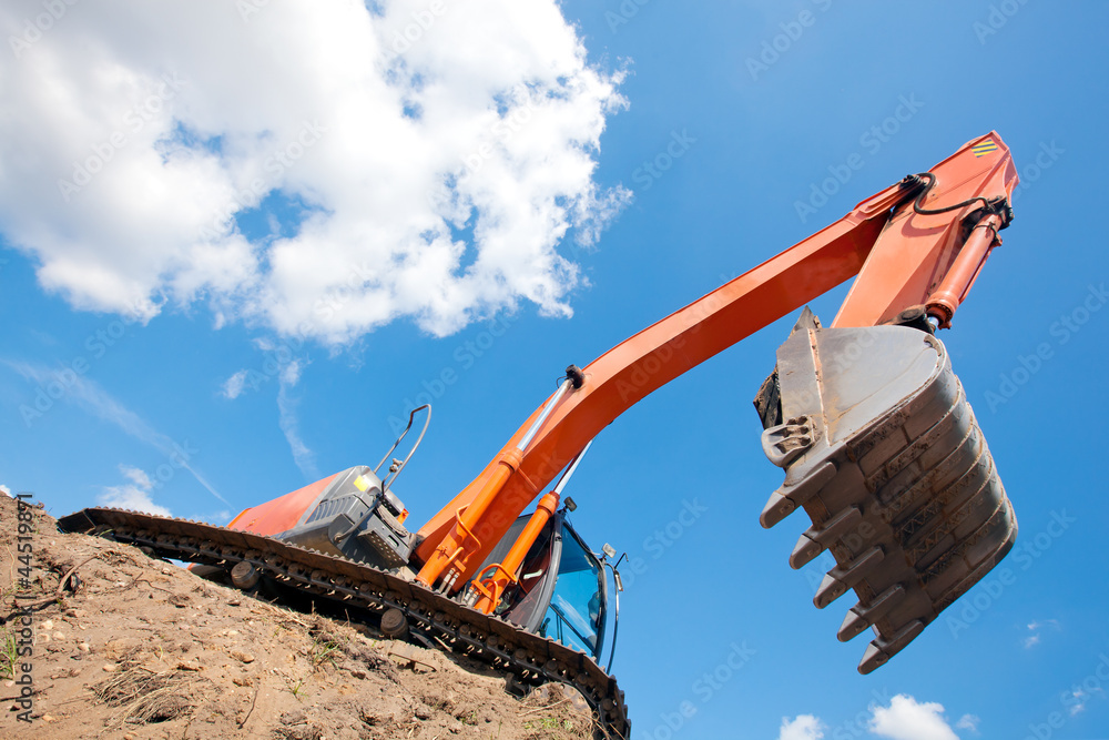 Fototapeta premium Excavator standing in a ground with raised bucket over sky