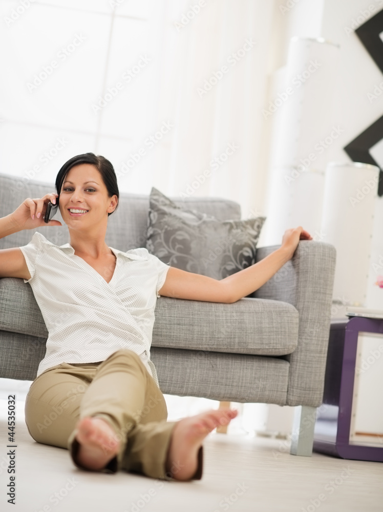 Happy young woman sitting on floor in living room and speaking m Happy young woman sitting on floor in living room and speaking m