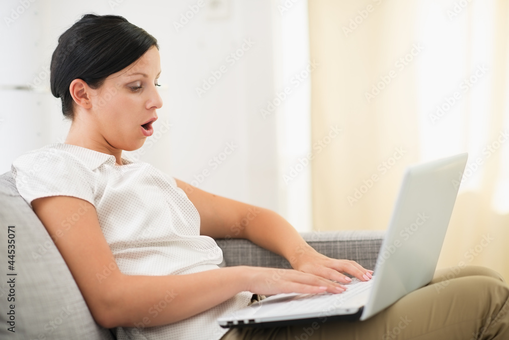 Surprised young woman using laptop in living room Surprised young woman using laptop in living room