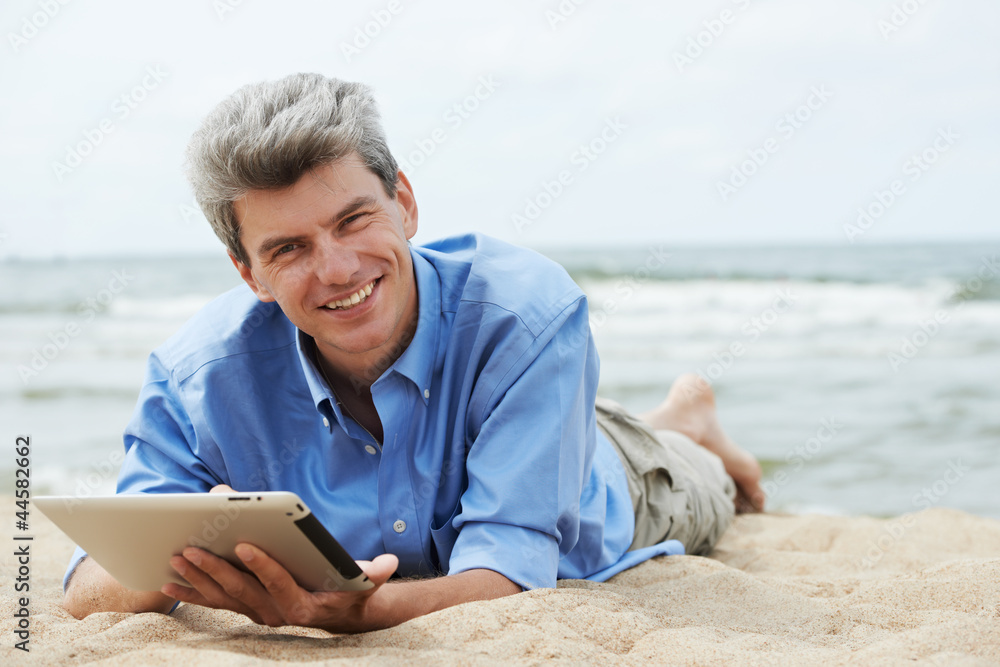 Young smiling man with tablet pc on seashore