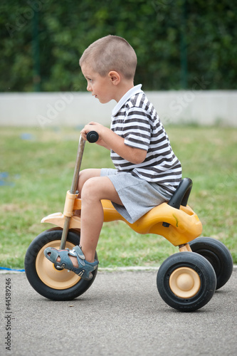 Four year old kid playing outdoor on tricycle.